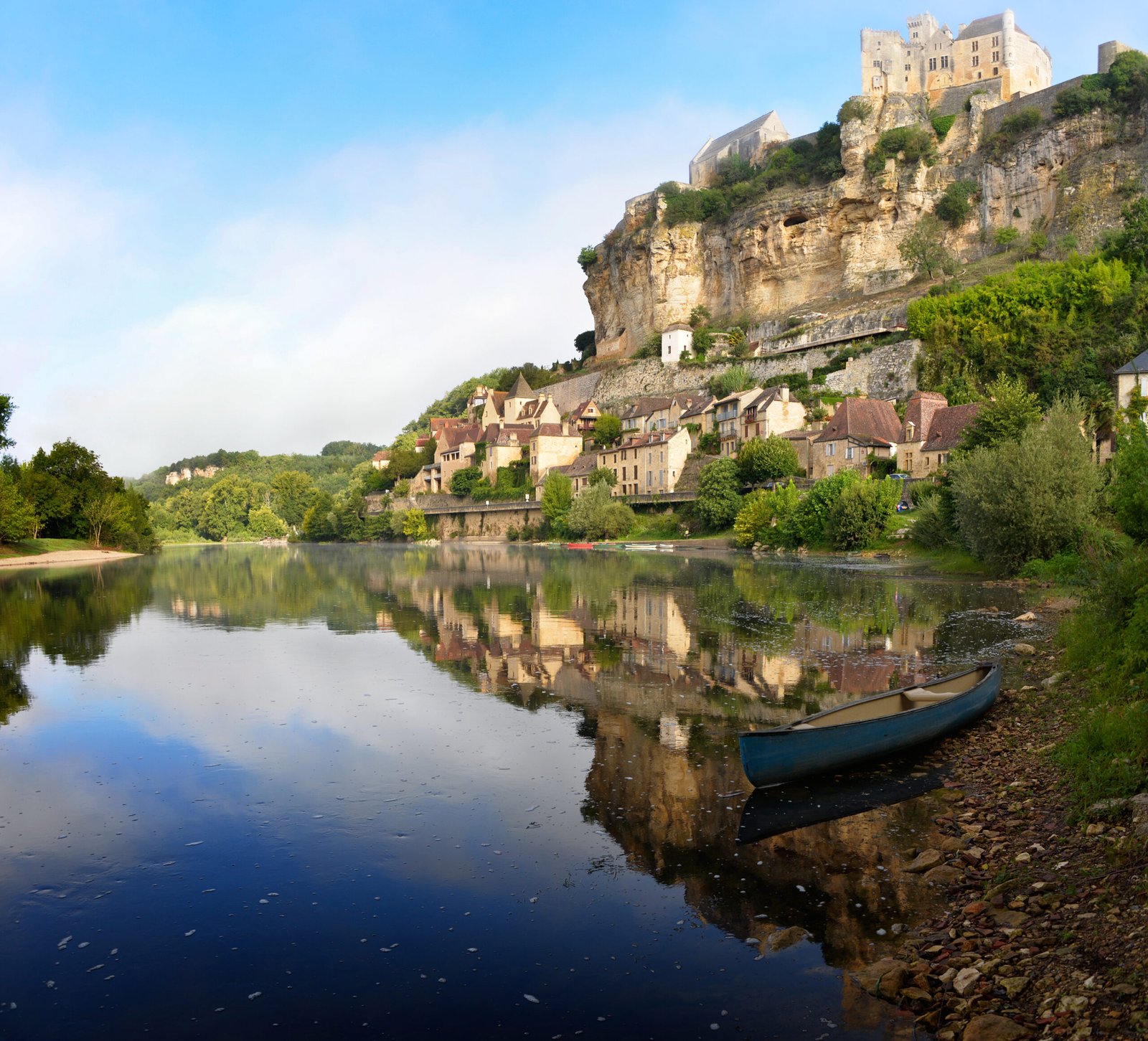 The beautiful village of Beynac-et-Cazenac with its characteristic Chateau de Beynac castle built upon the cliffs alongside Dordogne river in the early morning light with reflection in the water and a kayak in the foreground in the Perigord region in France.